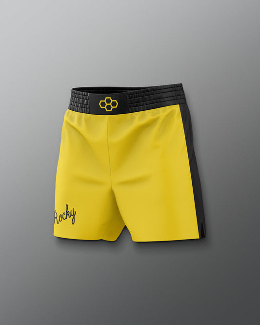 Yellow shorts with black waistband and 'Rocky' branding on a gray background