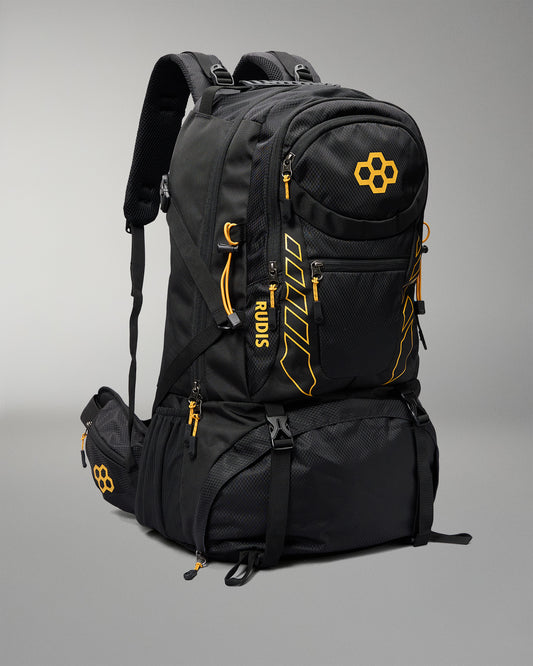 A black technical outdoor backpack with bright orange accents, zippers, and branding, shown on a neutral gray studio background.