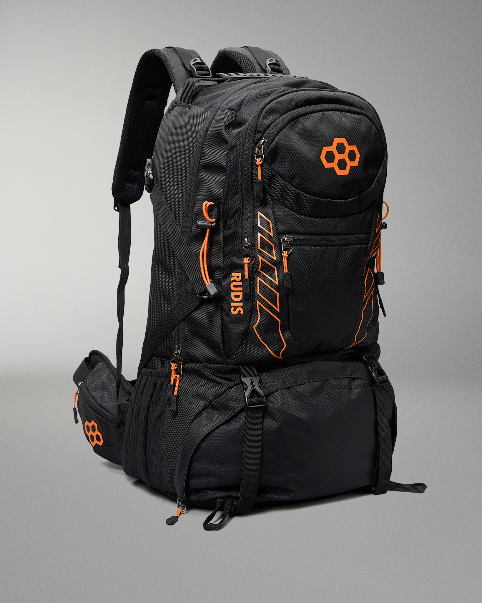 A black technical outdoor backpack with bright orange accents, zippers, and branding, shown on a neutral gray studio background.