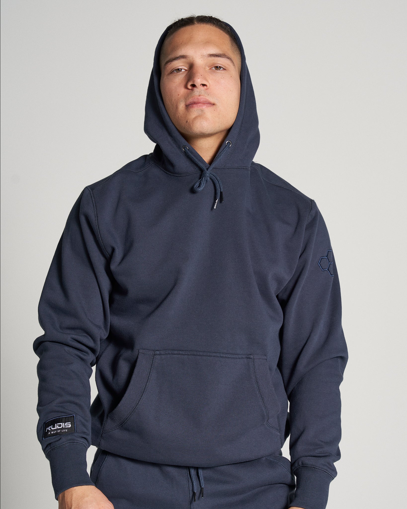 A young man wearing a navy hoodie with a front pocket and a casual confident expression posed against a plain light background