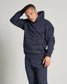 A young man poses confidently in a stylish navy blue hoodie and matching sweatpants featuring subtle branding and modern design elements