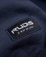 Close-up of a RUDIS brand logo on a navy fabric background that promotes a lifestyle centered around wrestling