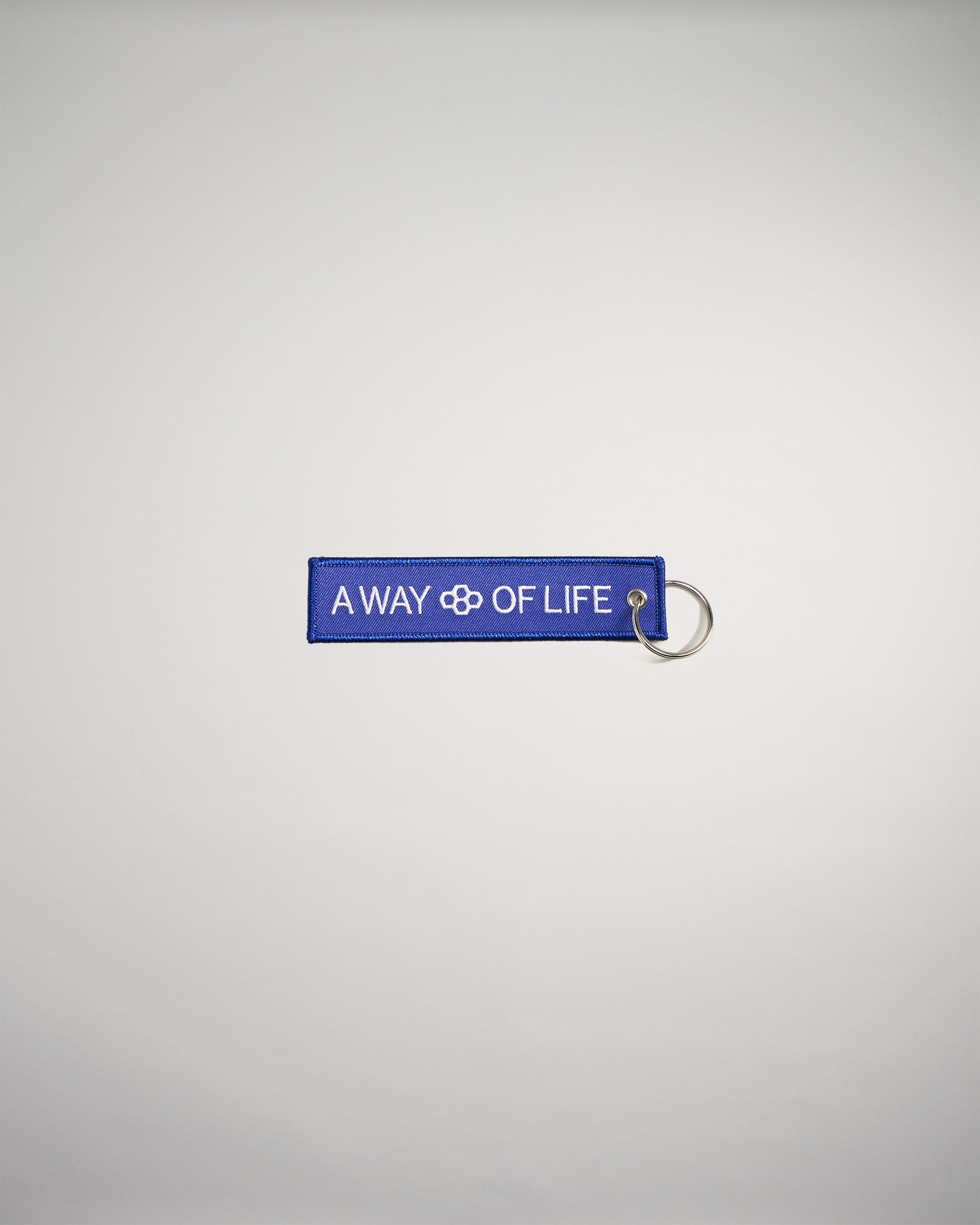 A vibrant blue keychain featuring the embroidered phrase A WAY OF LIFE in white text highlighting a simple yet impactful message