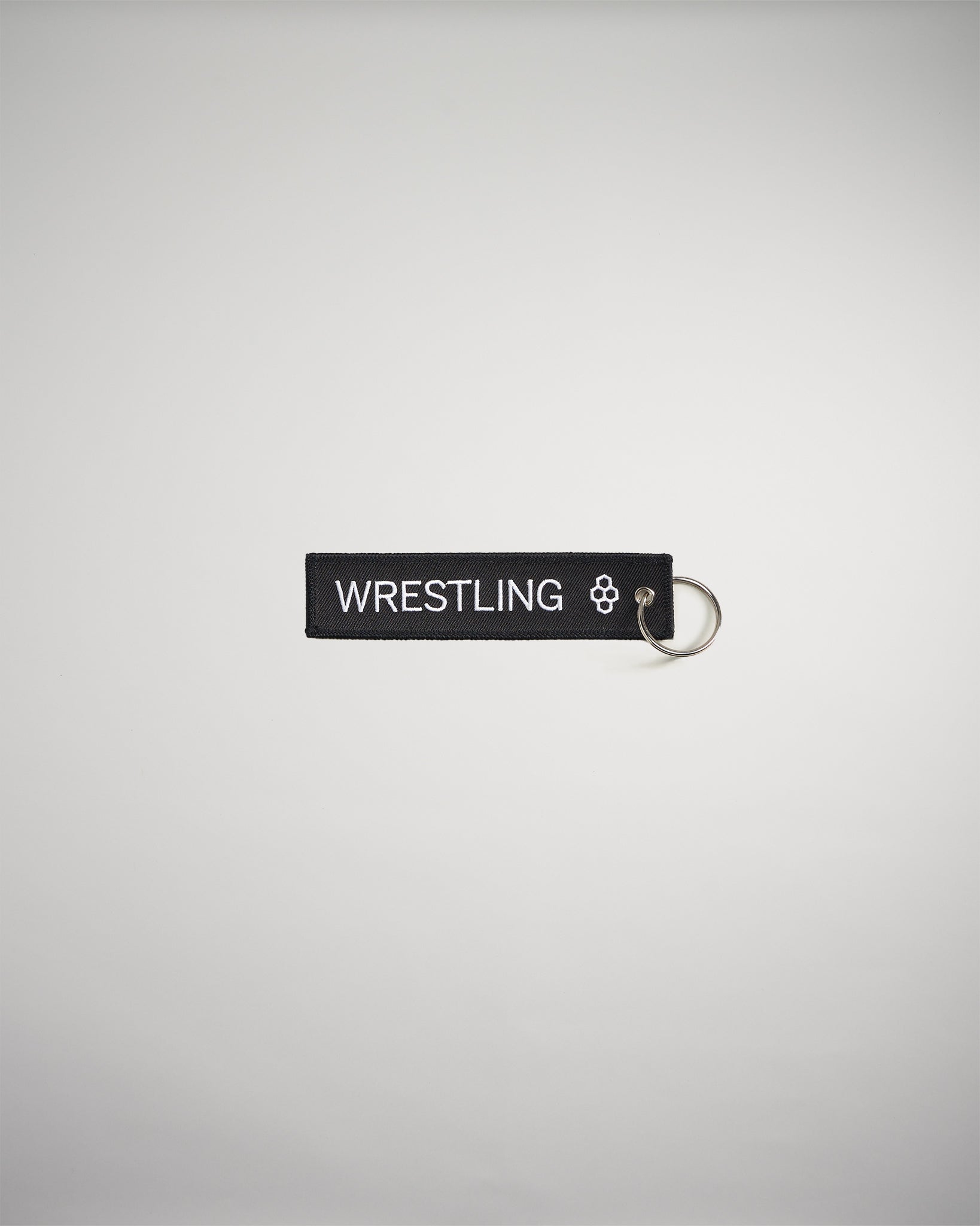A black keychain tag featuring the word WRESTLING in bold white letters attached to a silver metal ring