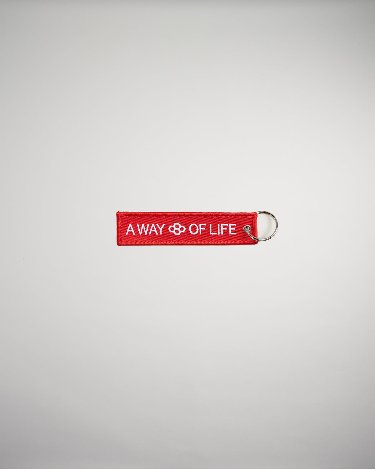 A red keychain tag featuring the phrase A WAY OF LIFE with a decorative symbol in the center designed to convey a lifestyle message