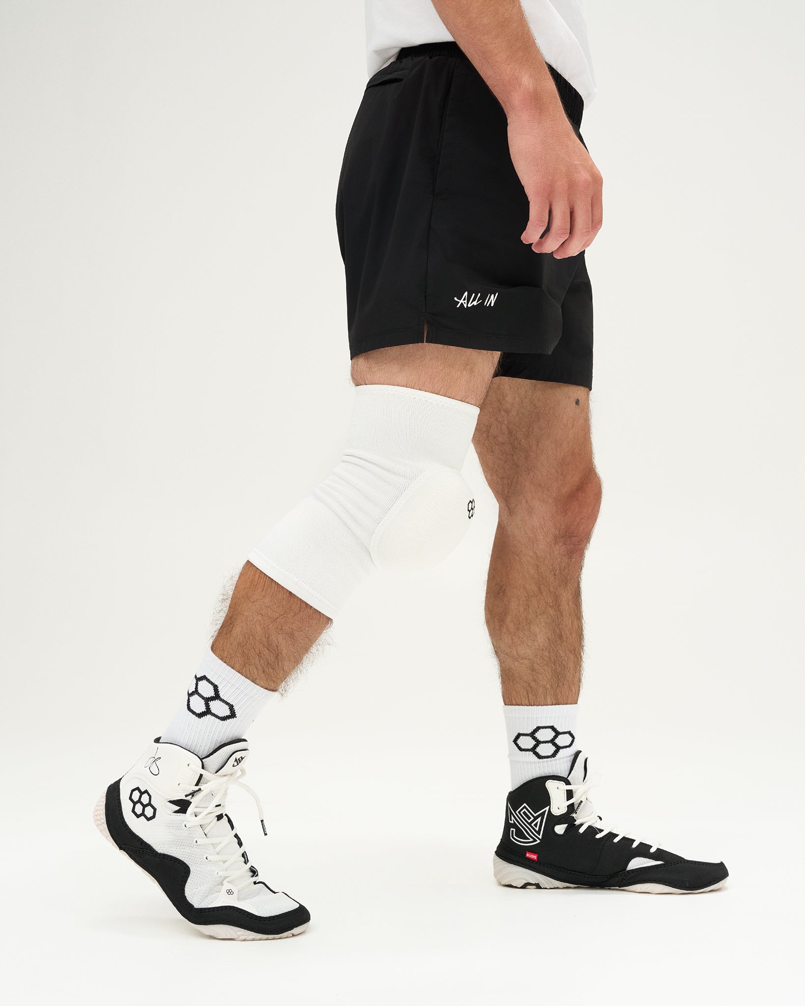 Person wearing a white knee pad and white sneakers with a quadhex design on a white background