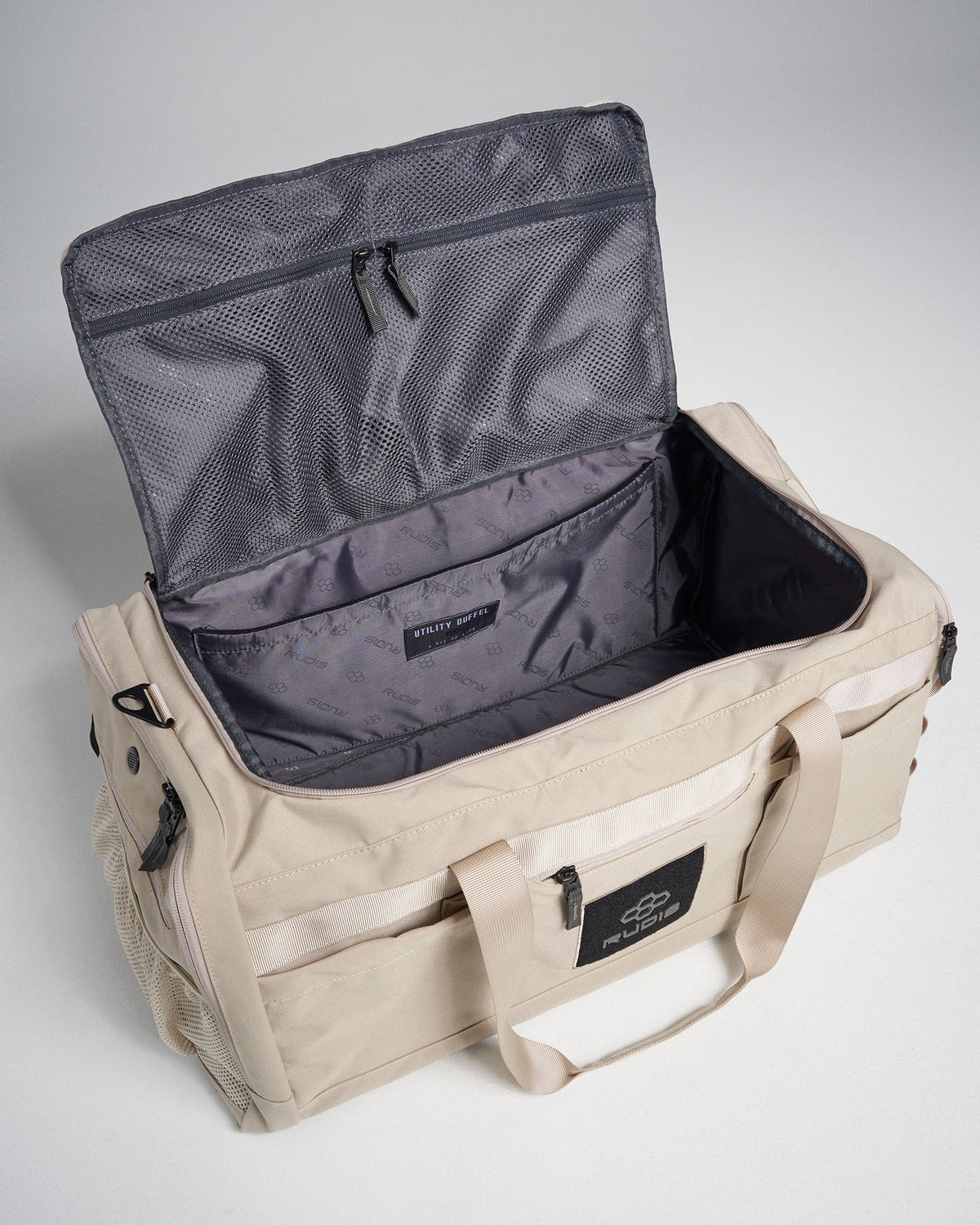 A light beige utility duffel bag with an open top showcasing ample storage space and a fine mesh pocket inside the lid