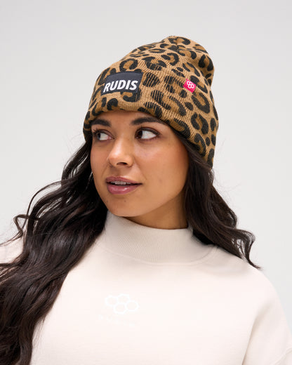 Female model wearing the RUDIS Leopard Foldover Beanie with a brown and black leopard print, ribbed foldover cuff, RUDIS logo patch and pink hex logo tag.