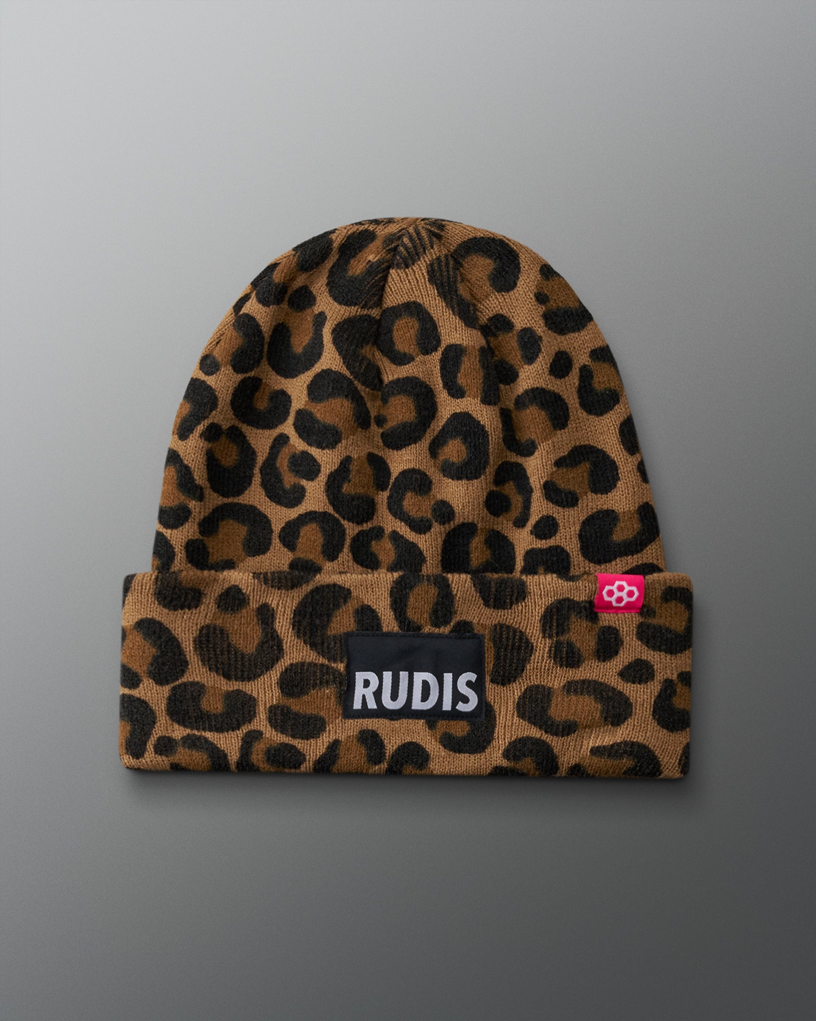 RUDIS Leopard Foldover Beanie featuring a brown and black leopard print knit design, folded cuff, black RUDIS logo patch, and pink wrestling logo tag, front view.