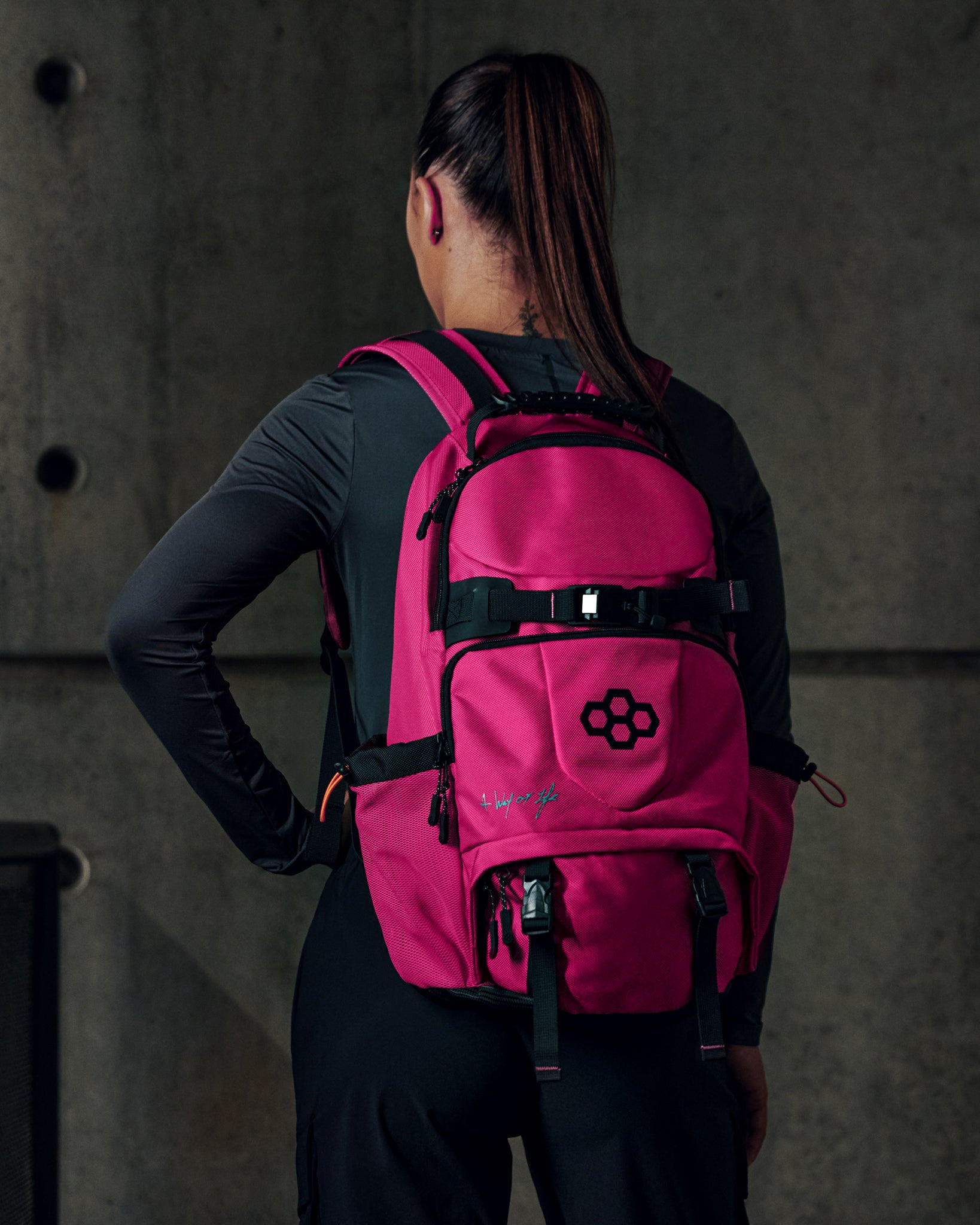 Person wearing a pink backpack with a logo on a dark background