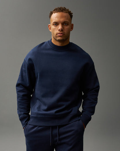 Man wearing a navy tracksuit with white sneakers on a gray background