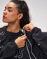 Woman wearing a black hoodie with white drawstrings against a plain background