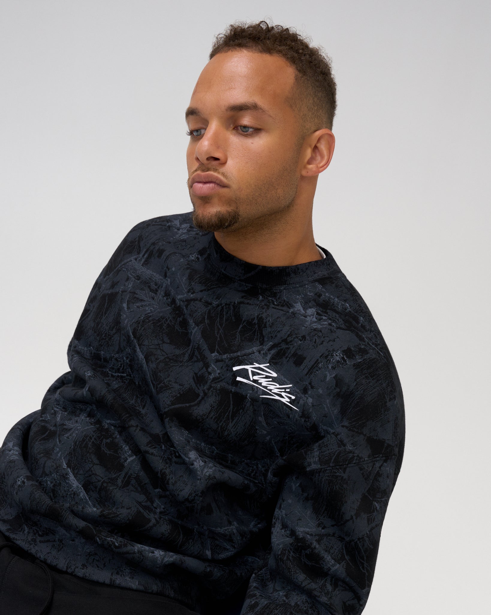 Close-up of man wearing the RUDIS Wrestling Relaxed Comfort Fleece Crewneck in Black Camo, highlighting the textured camo print and white chest logo.