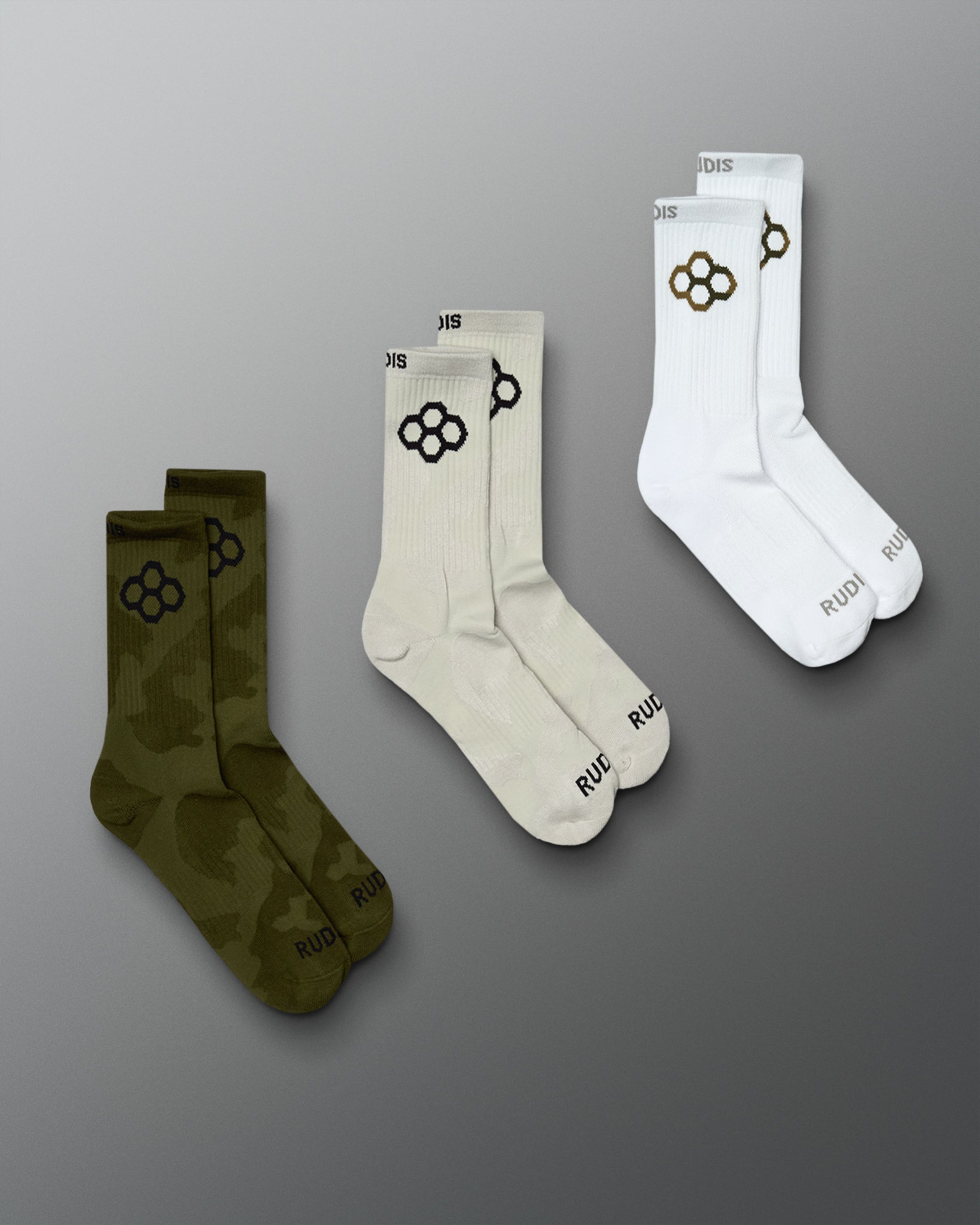 Three-pair assortment featuring Green Camo, White Camo, and White crew socks, each finished with the RUDIS Hex logo and RUDIS branding at the toe.