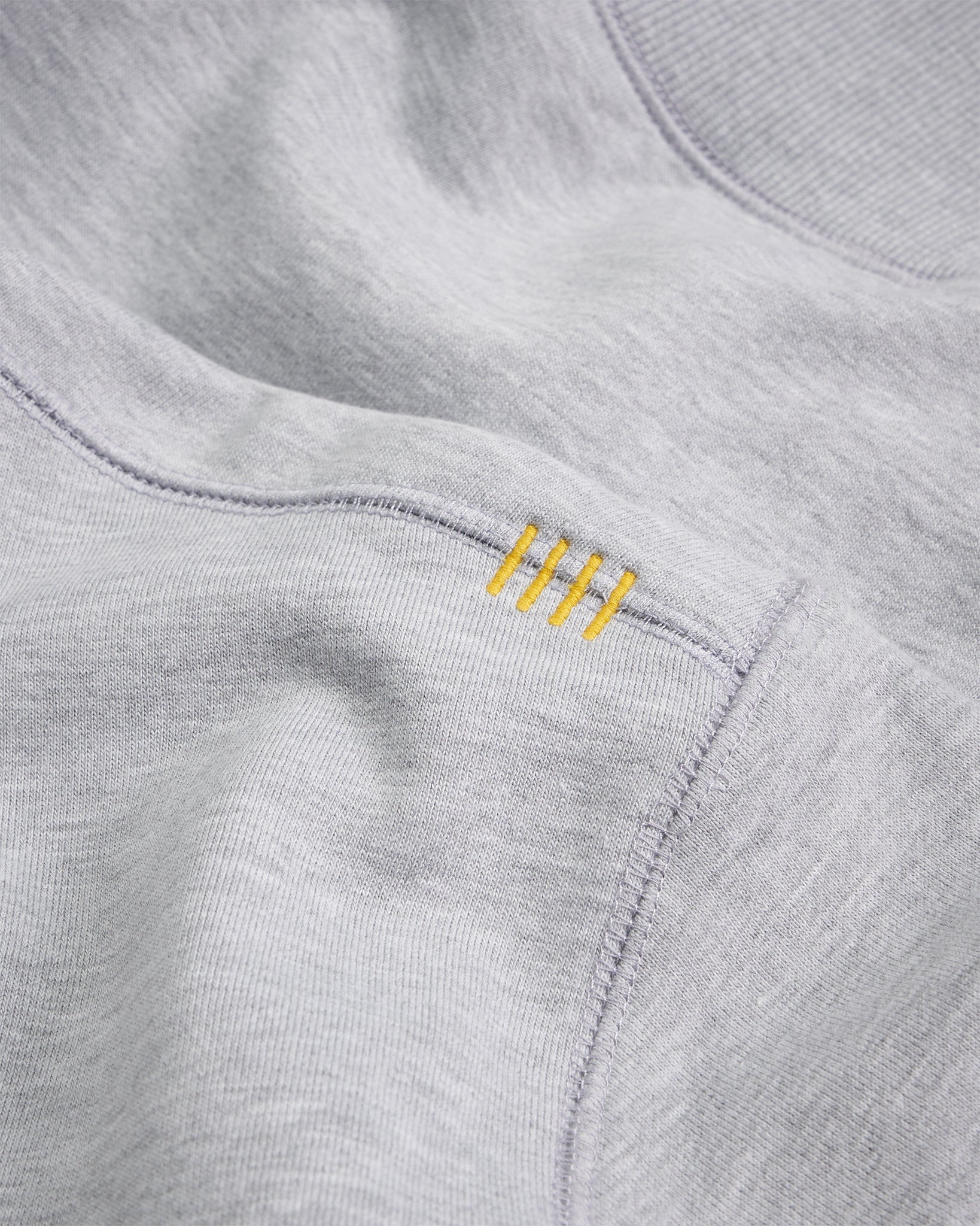 A close-up view of a light gray sweatshirt featuring unique yellow stitching accents on the side seam