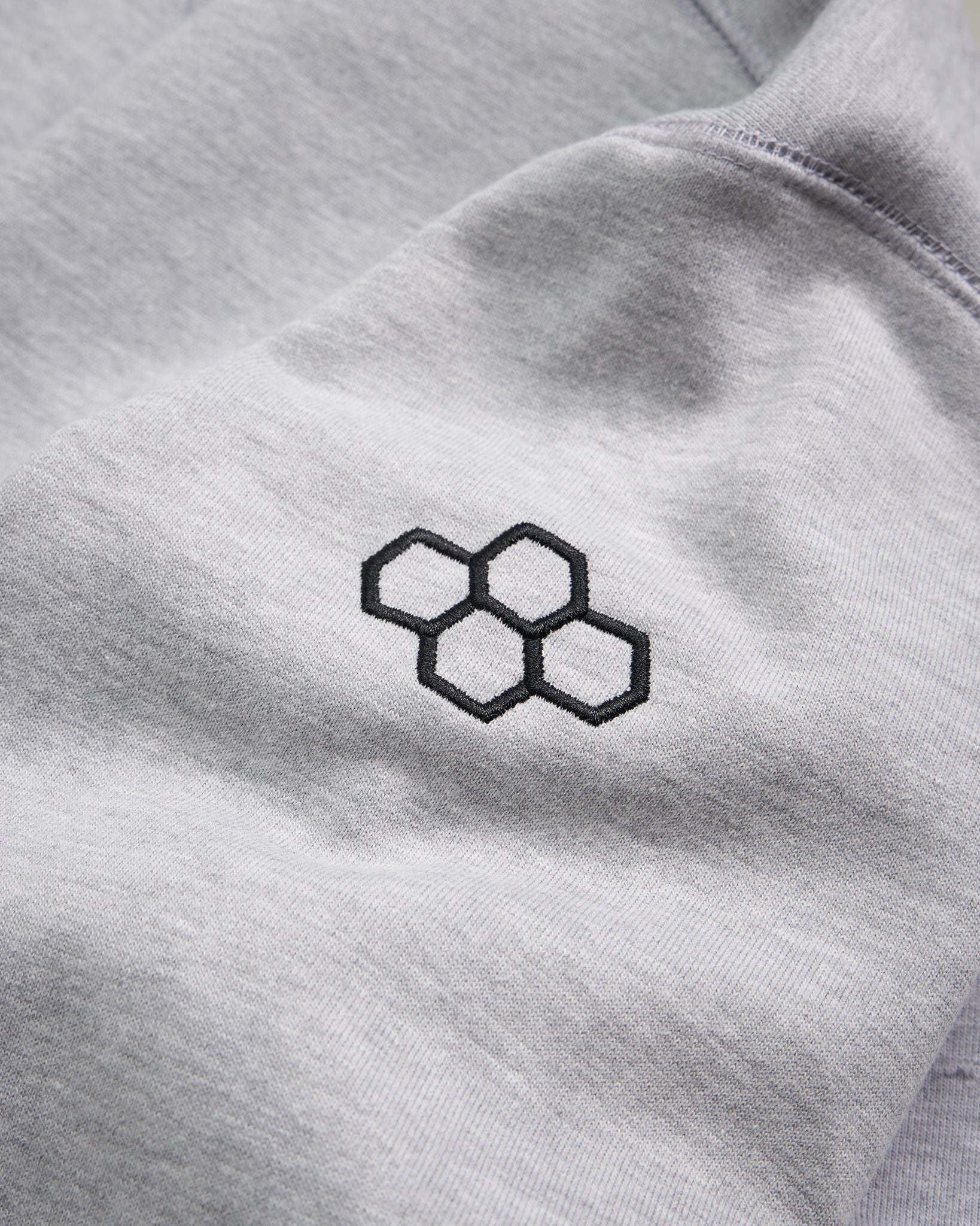 This image displays a close-up view of a grey fabric featuring an embroidered hexagonal logo in black conveying a modern and minimalist aesthetic
