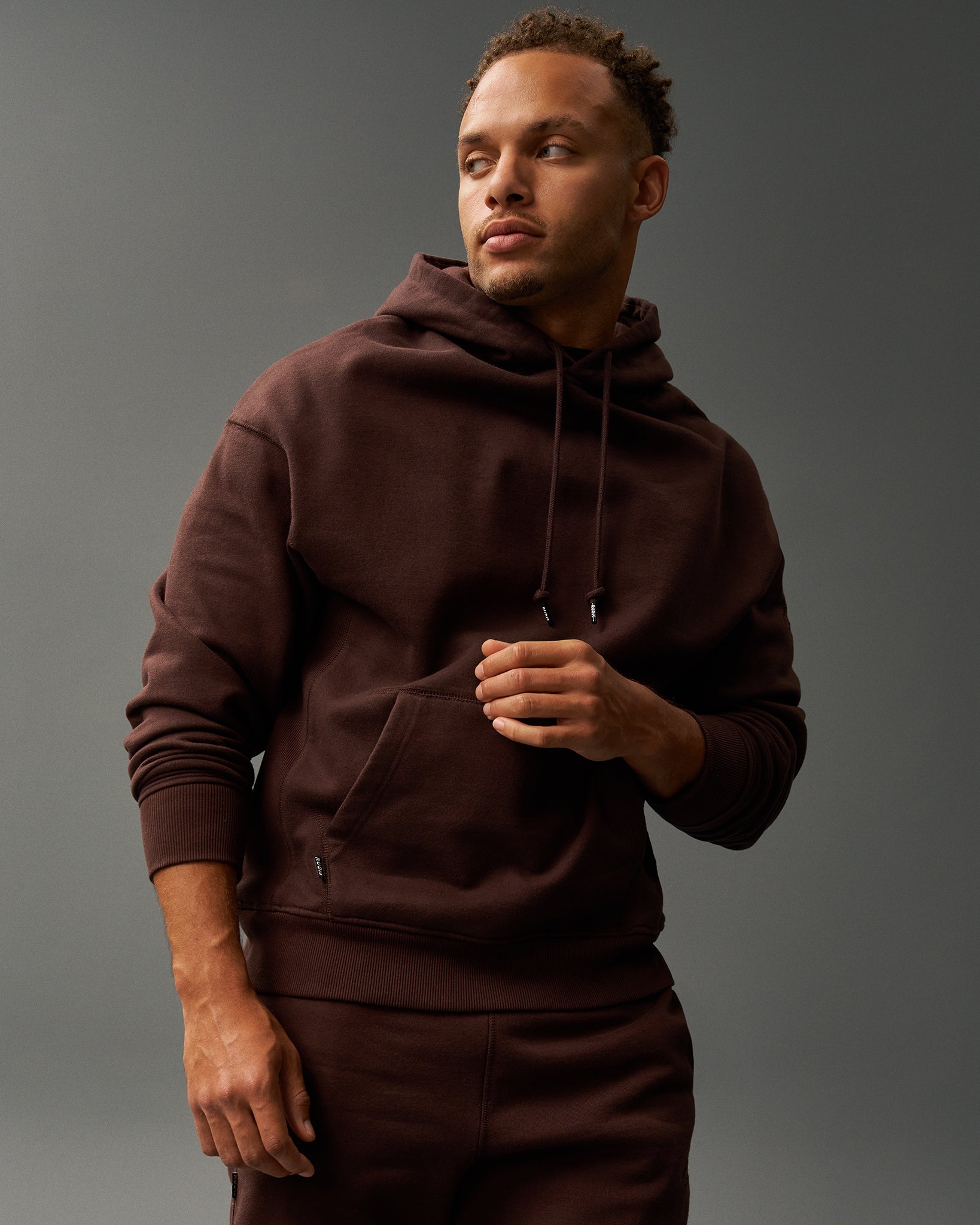 Man wearing a brown hoodie and pants against a gray background