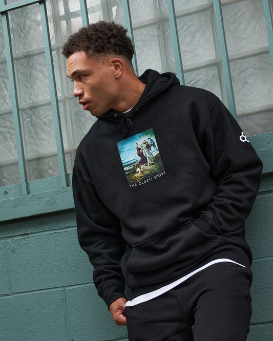 Person wearing a black hoodie with a graphic design, standing against a teal wall.