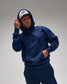 Man wearing a navy blue hoodie and pants with a white cap on a gray background