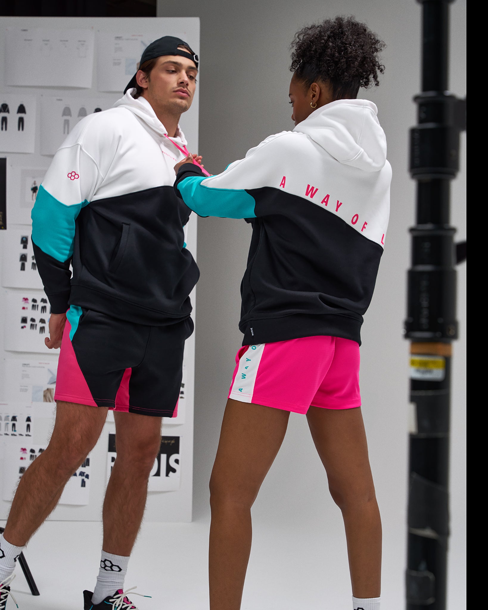 Two people wearing matching outfits with a brand logo in a studio setting.