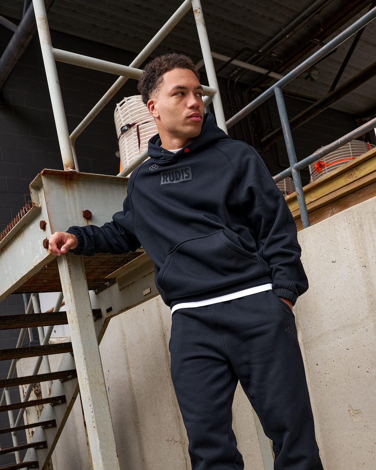 Person wearing a dark hoodie and pants standing on a metal staircase.