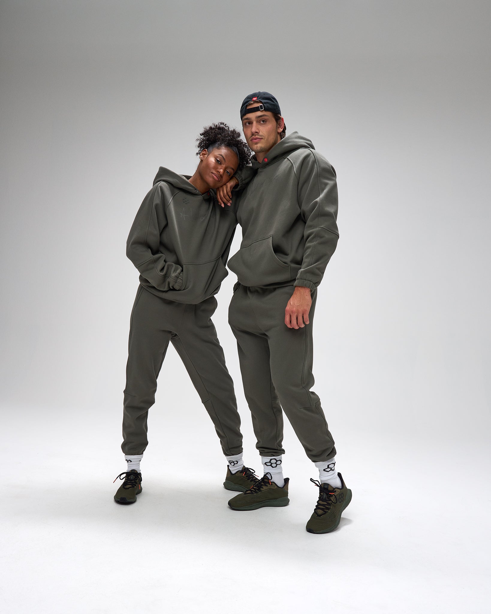 Two people wearing matching gray hoodies and pants on a white background