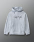 A light gray heather pullover hoodie with a kangaroo pocket and drawstring hood, featuring the text 'A way of life' printed in black script across the chest and a small circular logo on the left chest, shown against a dark gray gradient background.