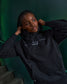Person wearing a black hoodie with text, sitting on steps against a green wall.