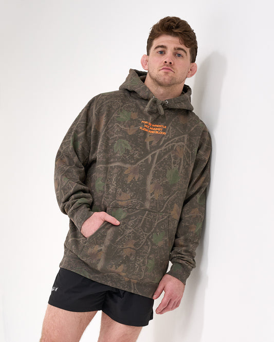 Man wearing a camouflage hoodie with orange 'For we wrestle not against flesh and blood' text on a white background