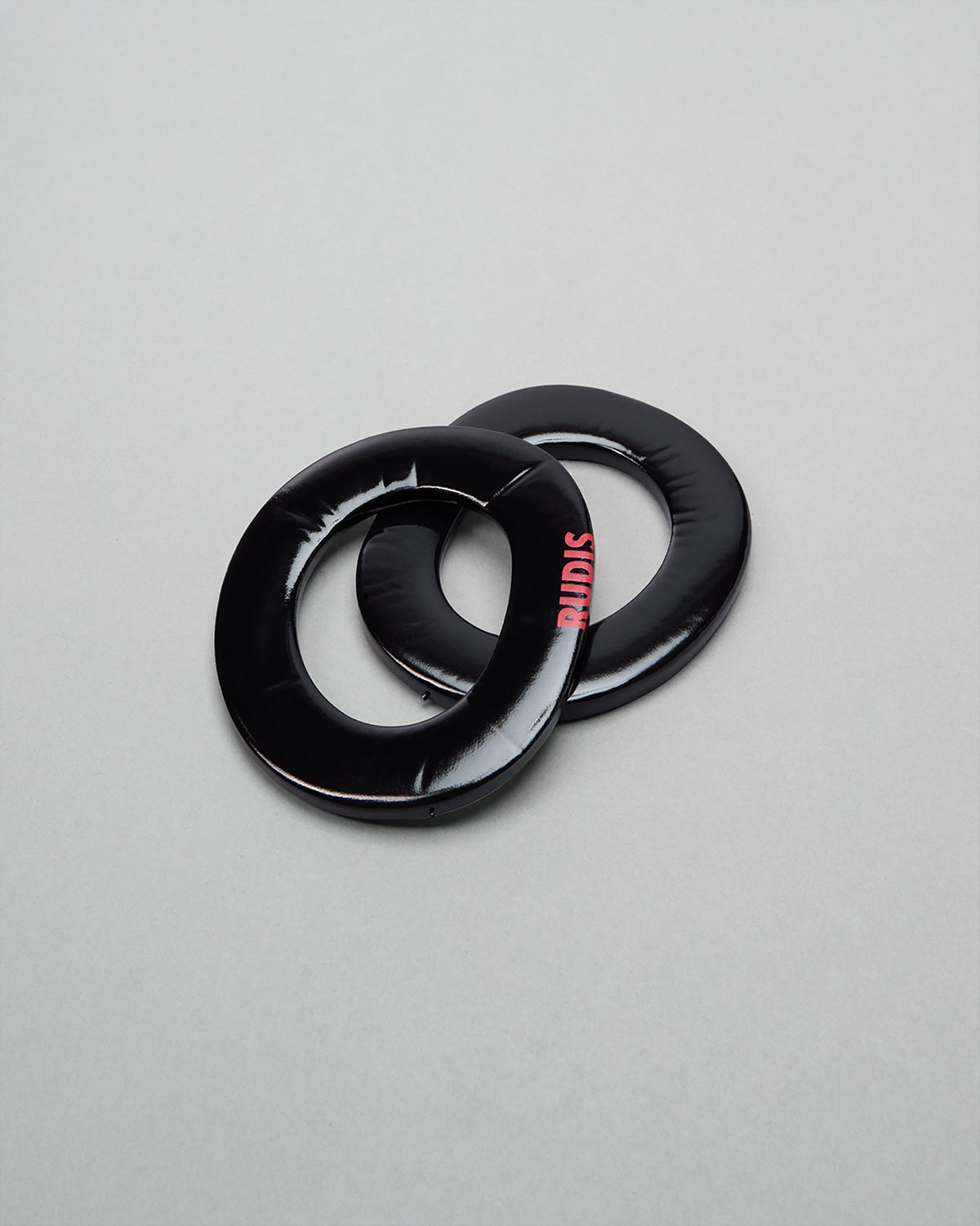 Two black wrestling headgear extension pads with 'RUDIS' branding on a gray background on a gray background