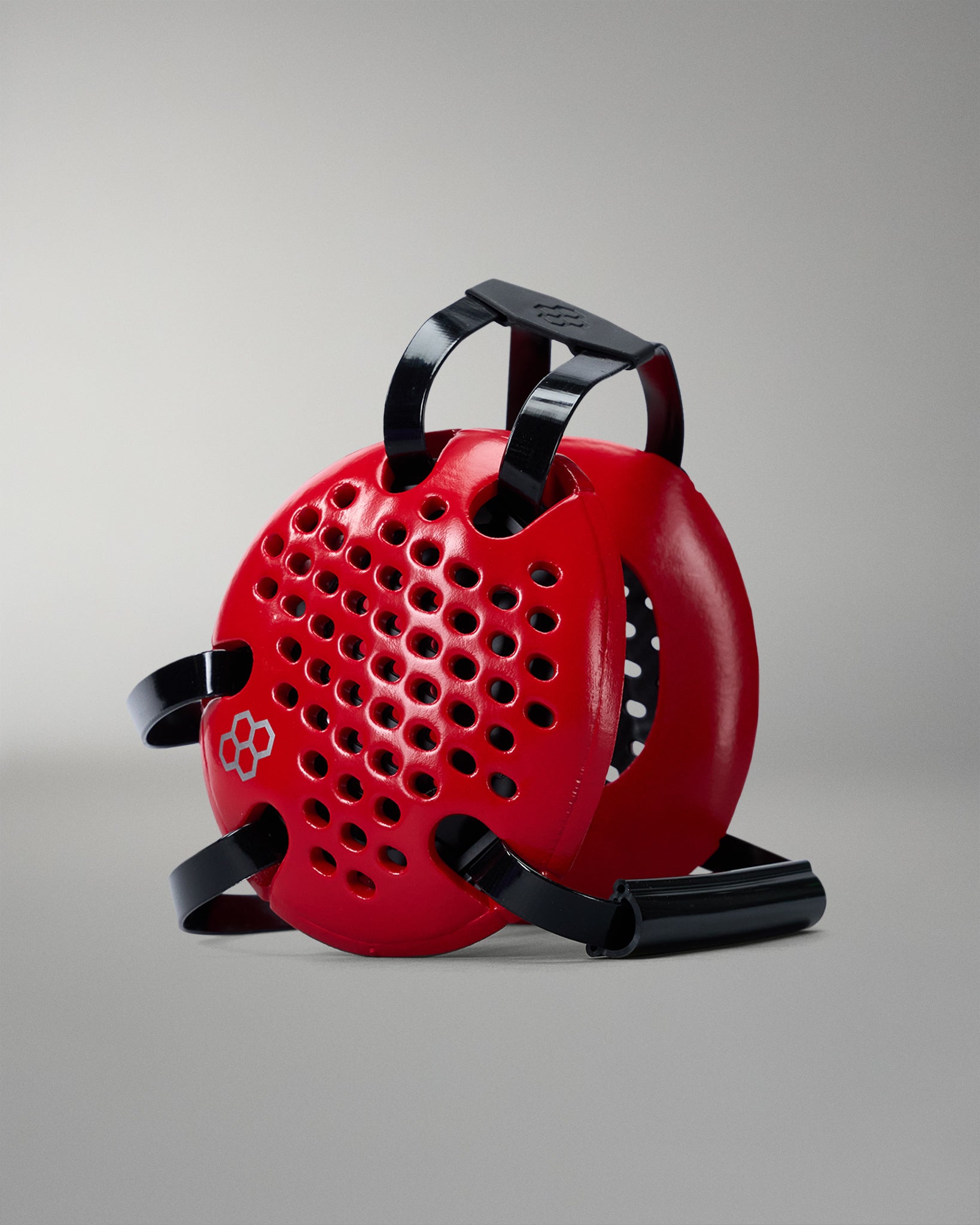 Red wrestling headgear with black handle and straps on a gray background
