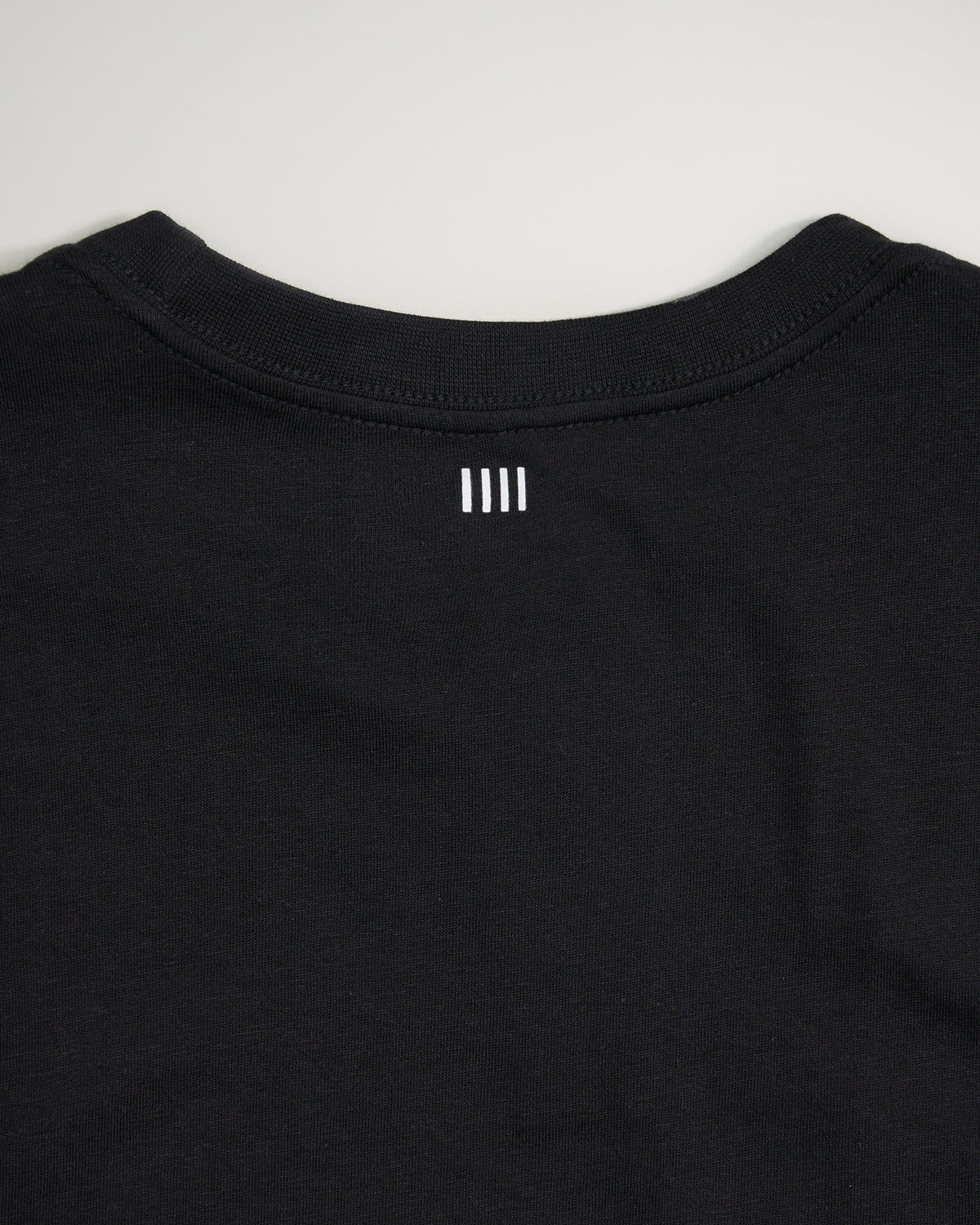 A close-up view of the back of a black t-shirt featuring a minimalist white logo design positioned below the neckline