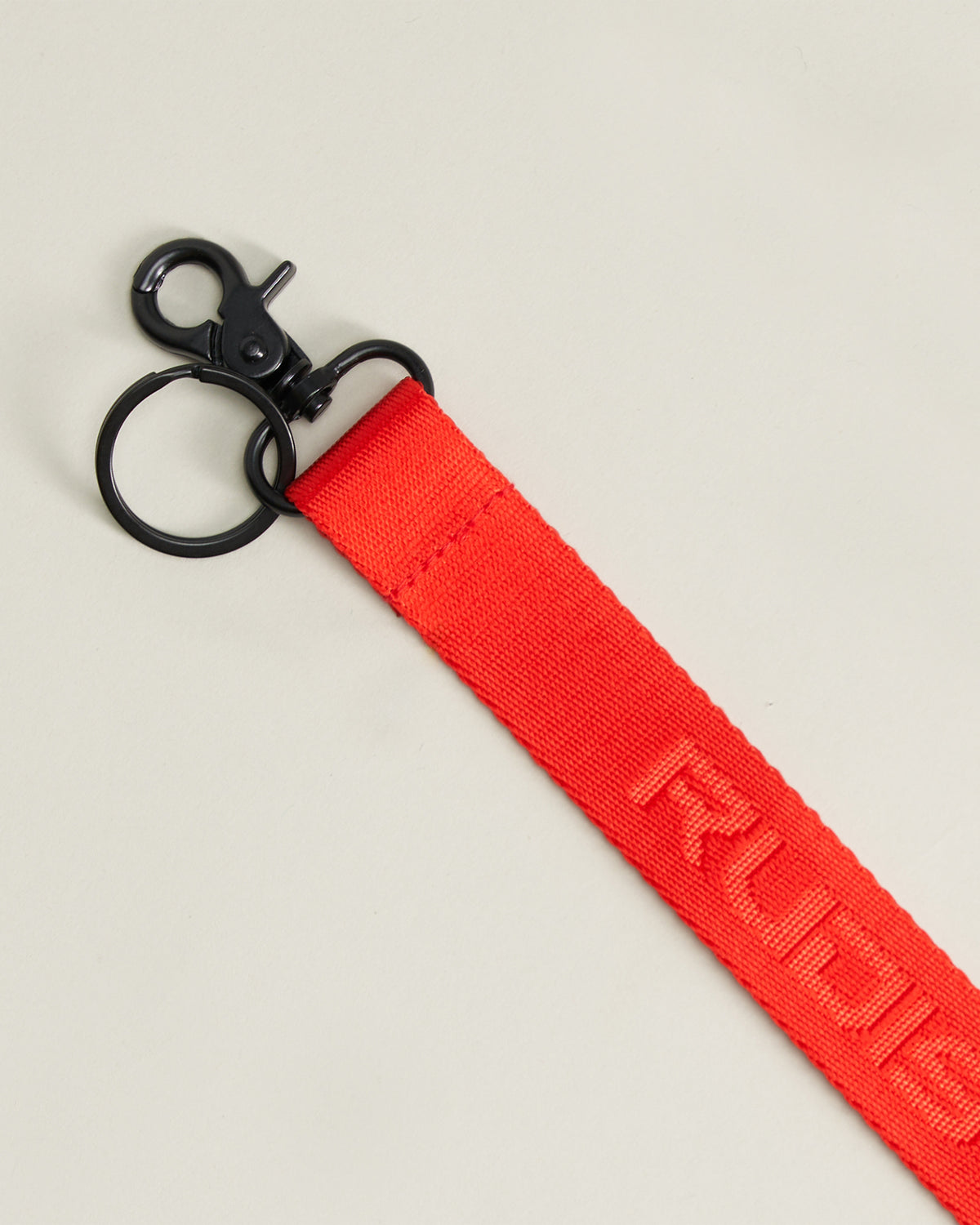 A vibrant red strap featuring a durable metal clip at one end and embossed lettering that reads RUDIS