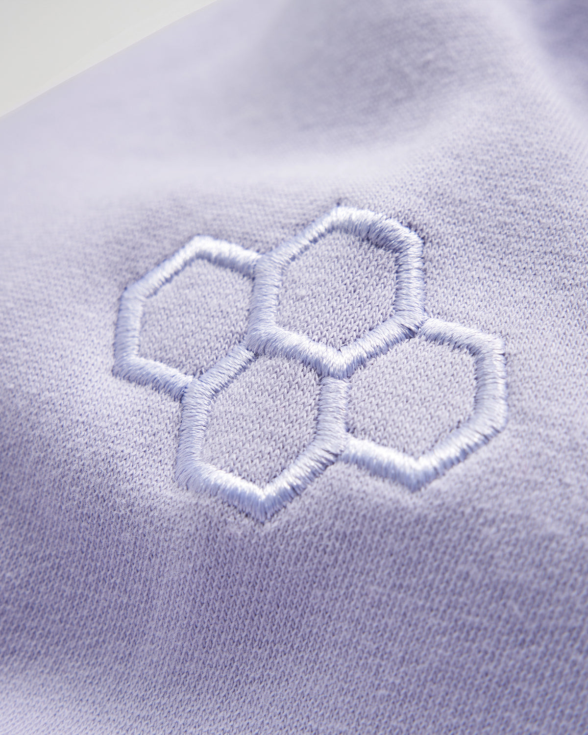 A close-up view of a light lavender fabric featuring a subtle embroidered hexagonal pattern