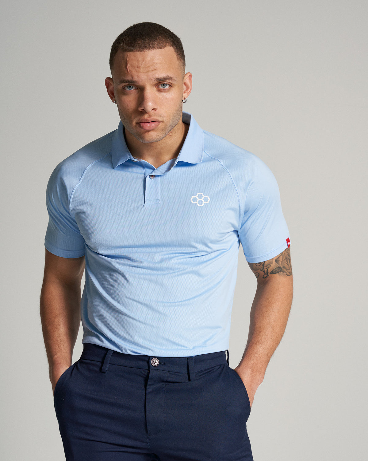 A man with a focused expression wears a light blue polo shirt and dark navy pants showcasing a casual yet stylish look