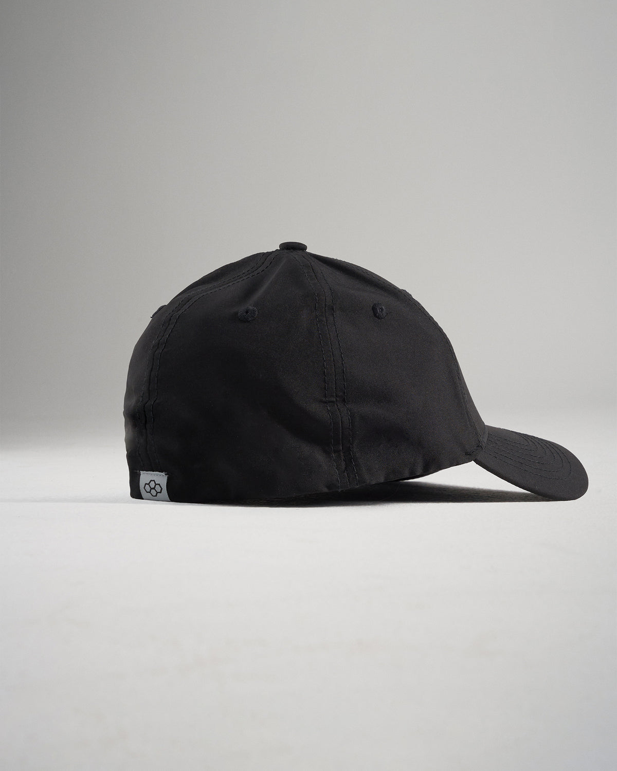 A black baseball cap viewed from the side featuring a curved visor and a signature tag on the back