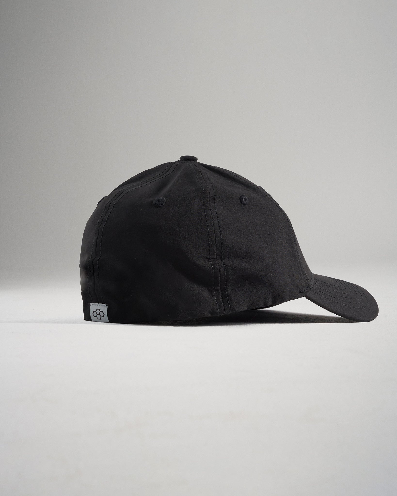 A black baseball cap viewed from the side featuring a curved visor and a signature tag on the back