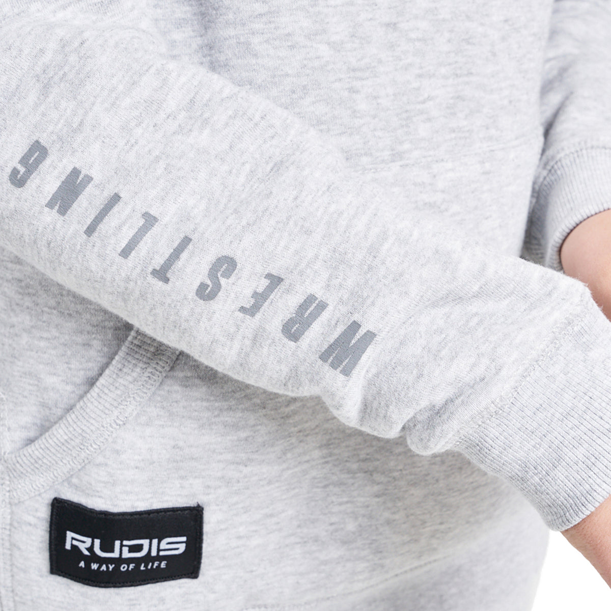 A close-up view of a light gray sweatshirt sleeve featuring the word WRESTLING printed vertically in bold gray letters and a black label for the brand RUDIS