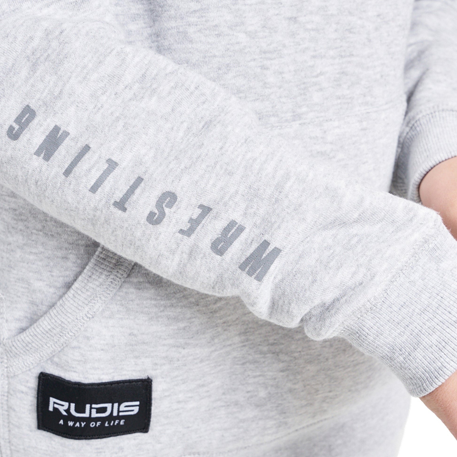 A close-up view of a light gray sweatshirt sleeve featuring the word WRESTLING printed vertically in bold gray letters and a black label for the brand RUDIS