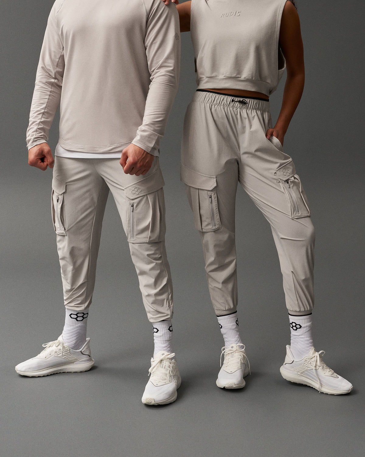 Two people wearing matching light gray outfits on a dark gray background