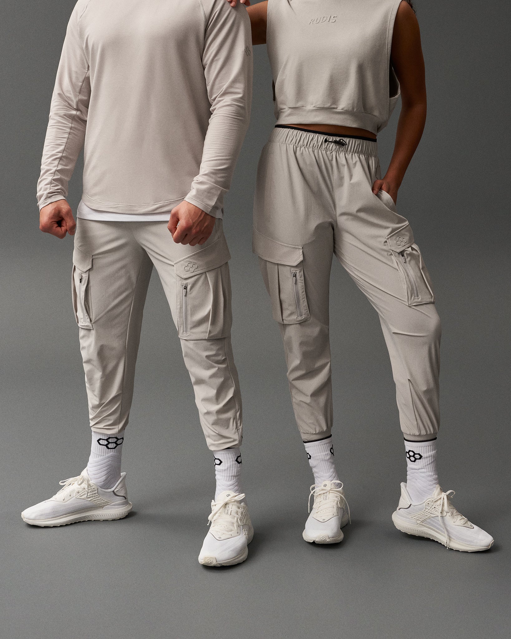 Two people wearing matching light gray outfits on a dark gray background