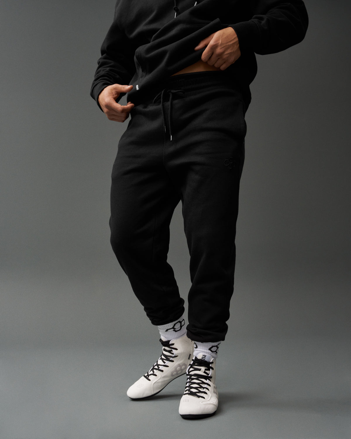 Person wearing a black tracksuit with white sneakers on a gray background