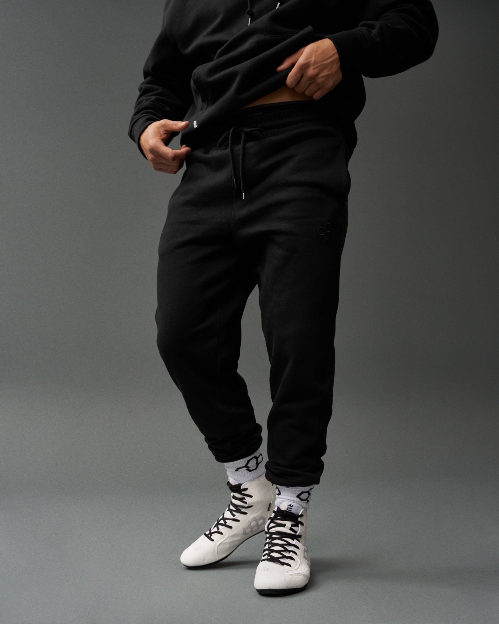 Person wearing a black tracksuit with white sneakers on a gray background