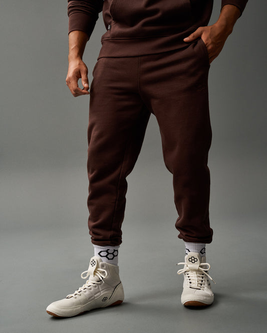 Person wearing brown tracksuit and white sneakers on a gray background
