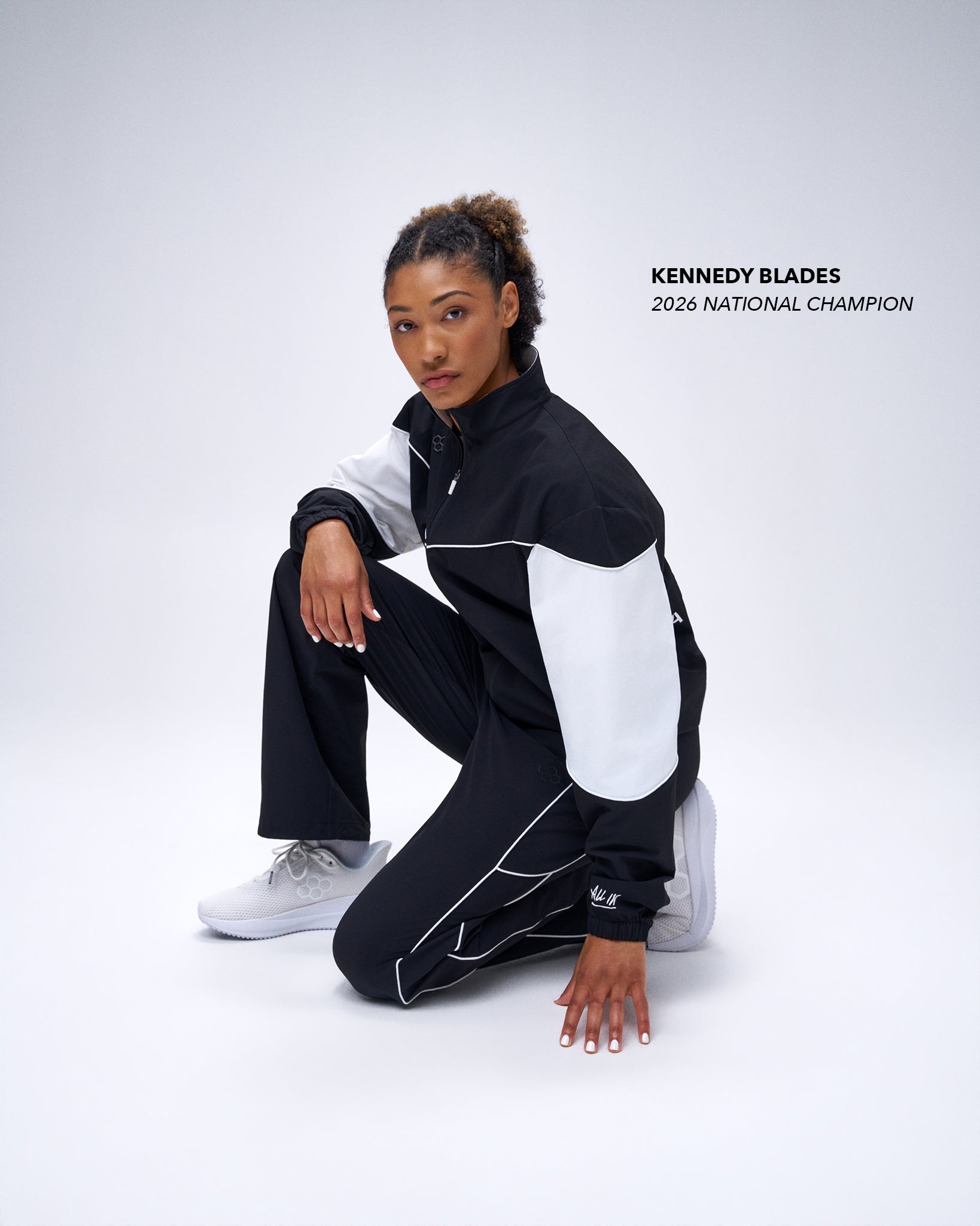 Model wearing black RUDIS Movement Podium Pants in a kneeling pose, showcasing the relaxed athletic fit and white piping details.