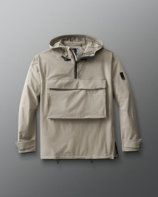 A beige, 1/4 zip jacket with a hood, designed for adults. The jacket features a front gear pocket, adjustable cuffs, hood, and waist, and is displayed on a grey background.