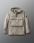 A beige, 1/4 zip jacket with a hood, designed for adults. The jacket features a front gear pocket, adjustable cuffs, hood, and waist, and is displayed on a grey background.