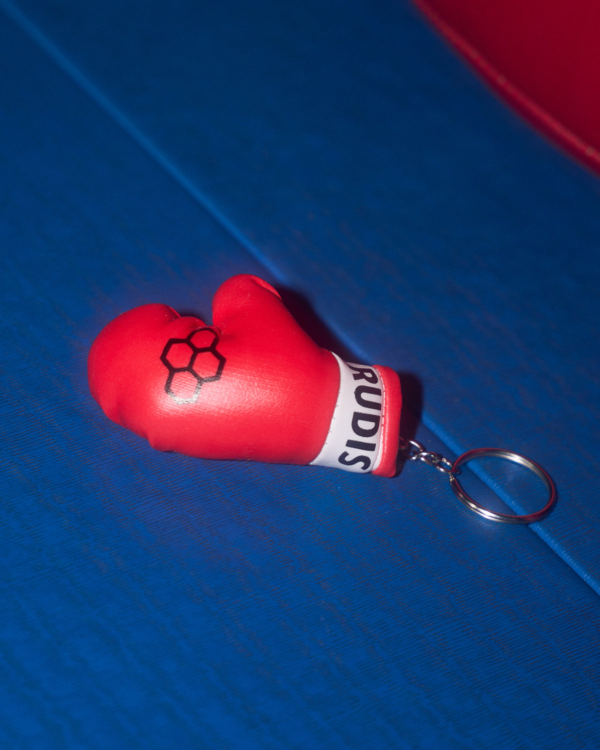 Red boxing glove keychain with 'Rudis' branding on a blue surface