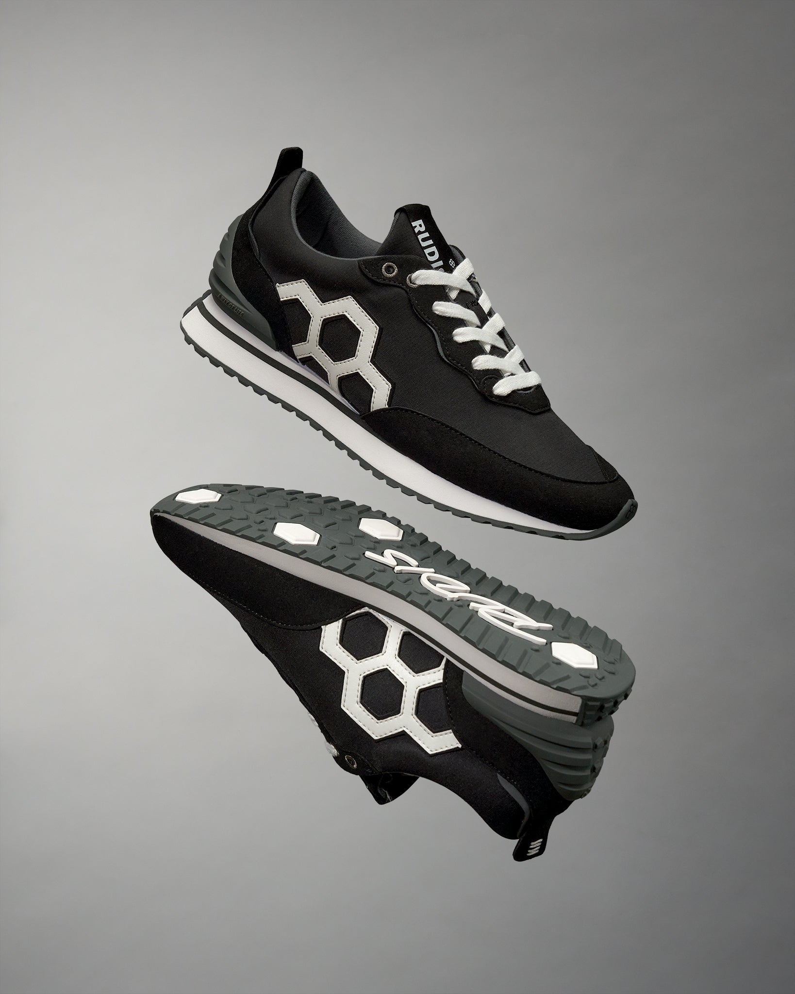 A pair of black RUDIS street lifestyle shoes with a prominent white hexagonal logo on the side, displayed against a grey background.