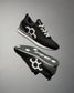 A pair of black RUDIS street lifestyle shoes with a prominent white hexagonal logo on the side, displayed against a grey background.